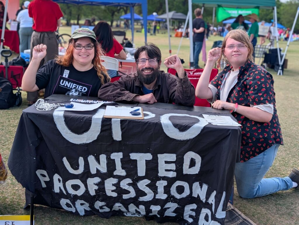 UPO leadership stands behind a hand-painted sign, raising their fists.