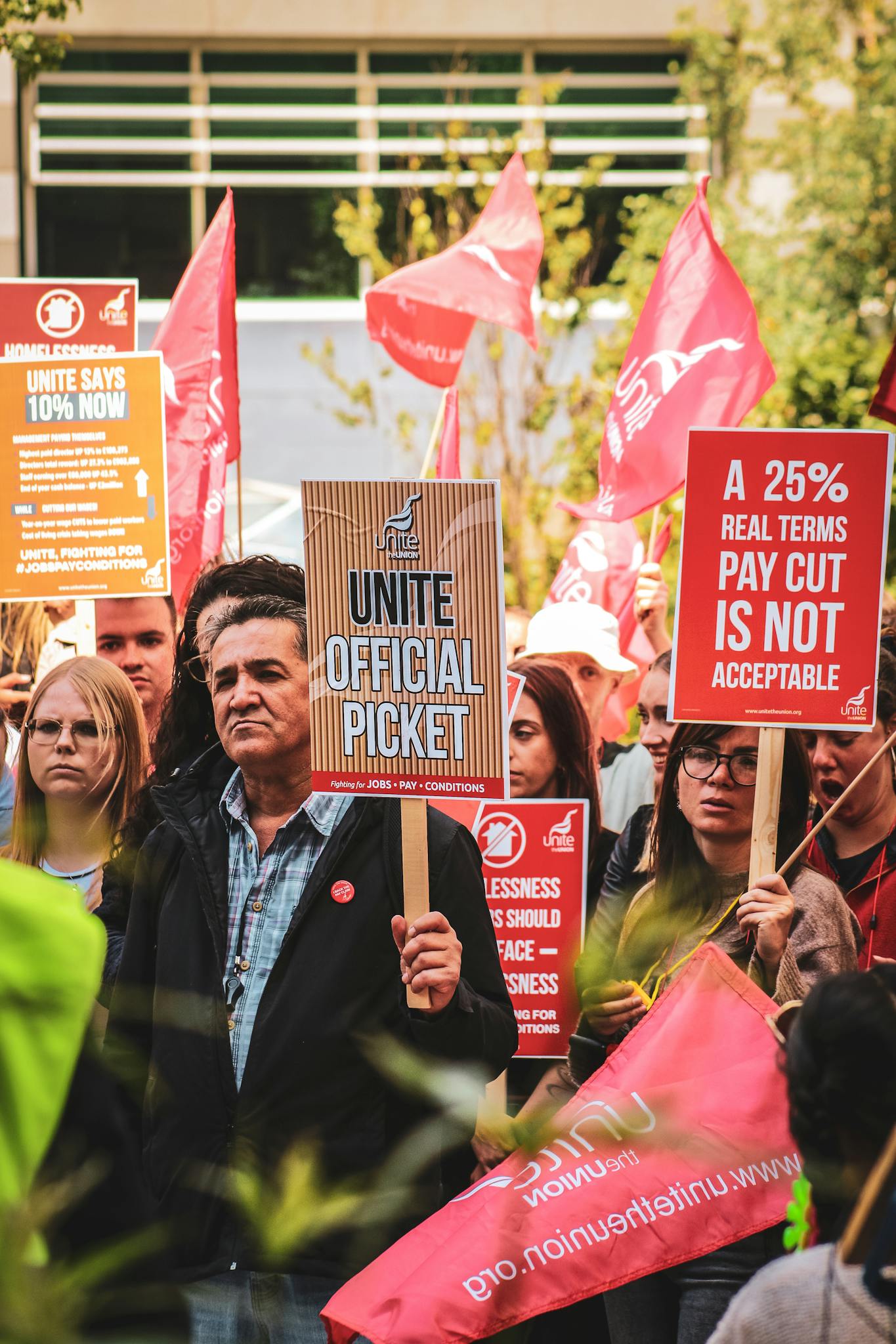 Group of people in London protesting against wage cuts, holding signs demanding fair pay.