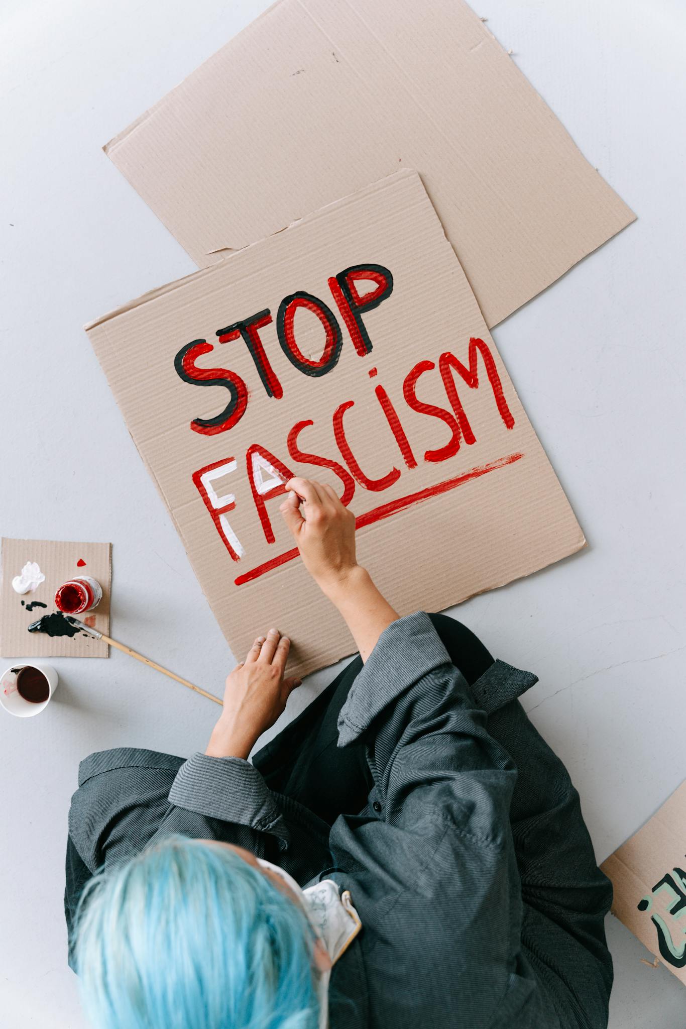 Overhead view of a protester painting 'Stop Fascism' on a cardboard sign.